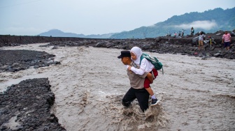 Personel Polsek Candipuro menggendong siswa sekolah dasar untuk menyeberangi aliran lahar hujan Gunung Semeru di Desa Jugosari, Kecamatan Candipuro, Lumajang, Jawa Timur, Selasa (24/2/2026). [ANTARA FOTO/Irfan Sumanjaya/tom]
