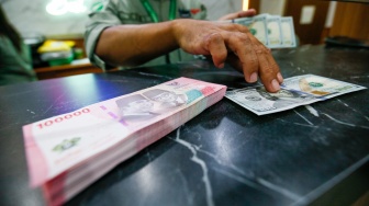 Petugas salah satu tempat penukaran mata uang asing menunjukkan uang rupiah dan dollar AS di Jakarta, Selasa (19/5/2026). [Suara.com/Alfian Winanto]