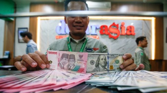 Petugas salah satu tempat penukaran mata uang asing menunjukkan uang rupiah dan dollar AS di Jakarta, Selasa (19/5/2026). [Suara.com/Alfian Winanto]