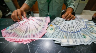 Petugas salah satu tempat penukaran mata uang asing menunjukkan uang rupiah dan dollar AS di Jakarta, Selasa (19/5/2026). [Suara.com/Alfian Winanto]