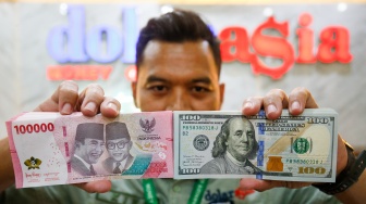 Petugas salah satu tempat penukaran mata uang asing menunjukkan uang rupiah dan dollar AS di Jakarta, Selasa (19/5/2026). [Suara.com/Alfian Winanto]