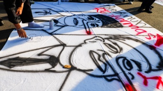 Pegiat HAM yang tergabung dalam Jaringan Solidaritas Korban menggambar karikatur saat mengikuti aksi kamisan ke-908 di seberang Istana Merdeka, Jakarta, Kamis (21/5/2026). [Suara.com/Alfian Winanto]
