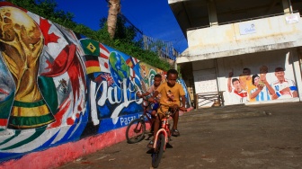 Dua anak bermain sepeda berlatar belakang mural Piala Dunia 2026 di Dok IX, Kelurahan Tanjung Ria, Jayapura Utara, Kota Jayapura, Papua, Senin (8/6/2026). [ANTARA FOTO/Gusti Tanati/sgd/wsj]
