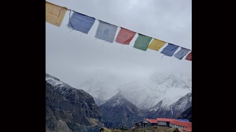 Bendera doa berwarna-warni berkibar di atas pos peristirahatan pendaki dengan latar belakang puncak gunung bersalju di Nepal, Jumat (29/5/2026). [Suara.com/Rizka Chaerani] 