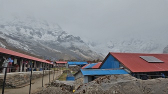 Seorang pendaki berjalan di area penginapan dengan latar belakang dinding es berselimut kabut di jalur trekking Annapurna Base Camp, Nepal, Jumat (29/5/2026). [Suara.com/Rizka Chaerani] 