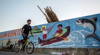 Seorang anak bersepeda di dekat tanggul pengaman pantai yang dihiasi mural bertema lingkungan di Kampung Bahari Tambaklorok, Semarang, Jawa Tengah, Kamis (23/7/2026). [ANTARA FOTO/Aprillio Akbar/foc]