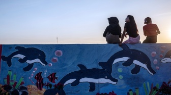 Sejumlah warga duduk di tanggul pengaman pantai yang dihiasi mural bertema lingkungan di Kampung Bahari Tambaklorok, Semarang, Jawa Tengah, Kamis (23/7/2026). [ANTARA FOTO/Aprillio Akbar/foc] 