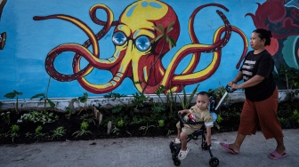 Warga berjalan di dekat mural bertema lingkungan di tanggul pengaman pantai Kampung Bahari Tambaklorok, Semarang, Jawa Tengah, Kamis (23/7/2026). [ANTARA FOTO/Aprillio Akbar/foc]