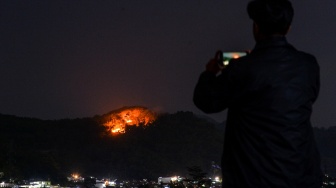 Seorang warga memotret kebakaran hutan yang terjadi di Gunung Jati, Desa Jatisari, Kecamatan Kutawaringin, Kabupaten Bandung, Jawa Barat, Senin (27/7/2026). [ANTARA FOTO/Raisan Al Farisi/tom]

