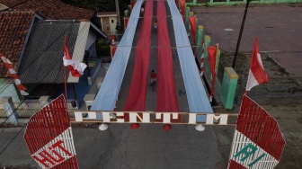 Foto udara seorang anak bersepeda di bawah bendera Merah Putih yang terbentang di Kampung Peundeuy Timur, Desa Karang Satu, Kecamatan Karangbahagia, Kabupaten Bekasi, Jawa Barat, Kamis (6/8/2026). [ANTARA FOTO/Darryl Ramadhan/kye]
