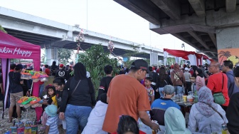 Warga menonton para peserta yang mengikuti lomba memanjat pohon pinang di Semarak Kalimalang 2026 di Jakarta, Senin (17/8/2026). [Suara.com/Novi]

