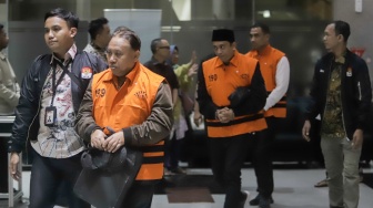 Rektor Universitas Jenderal Soedirman (Unsoed)  bersama tersangka lainnya berjalan menuju mobil tahanan usai menjalani pemeriksaan pasca terjaring operasi tangkap tangan (OTT) di Gedung KPK, Jakarta, Sabtu (22/8/2026) dini hari. [Suara.com/Alfian Winanto]
