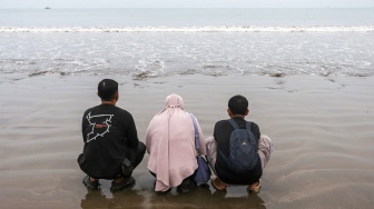 Istri dan anak jurnalis Merdeka.com yang hilang kontak, Arie Basuki, Yanti (tengah) dan Bintang (kanan) berdoa sebelum melakukan tabur bunga di bibir Pantai Kampung Pagedongan, Carita, Pandeglang, Banten, Jumat (18/9/2026). [ANTARA FOTO/Angga Budhiyanto/agr]