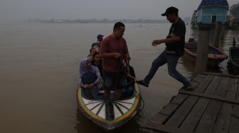 Tiga warga duduk di perahu motor di Sungai Kapuas yang diselimuti kabut asap pekat di Pontianak, Kalimantan Barat, Kamis (8/10/2026). [ANTARA FOTO/Jessica Wuysang/ky]