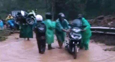 Seorang pria memanggul sepeda motornya menerobos jalanan tertutup longsor di Pujon Malang [Tangkapan Layar Facebook]