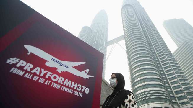 Seorang perempuan melintas di samping papan reklame yang bertuliskan \" Pray for MH370\" di Kuala Lumpur City Center, Jumat (14/3). [Reuters/Samsul Said] 