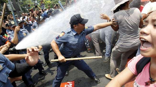 Seorang anggota polisi anti huru hara Filipina yang membawa tongkat mencoba menangkap seorang demonstran yang menolak kedatangan Presiden AS Barack Obama. (Reuters/Romeo Ranoco)