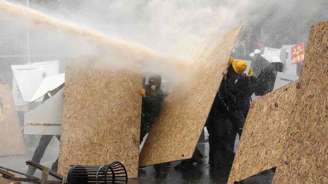 Demonstran berlindung dari siraman water cannon saat unjuk rasa Hari Buruh Internasional di Istanbul, Kamis (1/5). [Reuters/Murad Sezer]