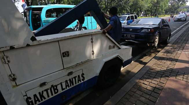 Petugas Polantas menertibkan kendaraan roda empat yang terparkir liar di sepanjang jalan Medan Merdeka Barat Jakarta, Senin (18/8). [suara.com/Kurniawan Mas'ud]