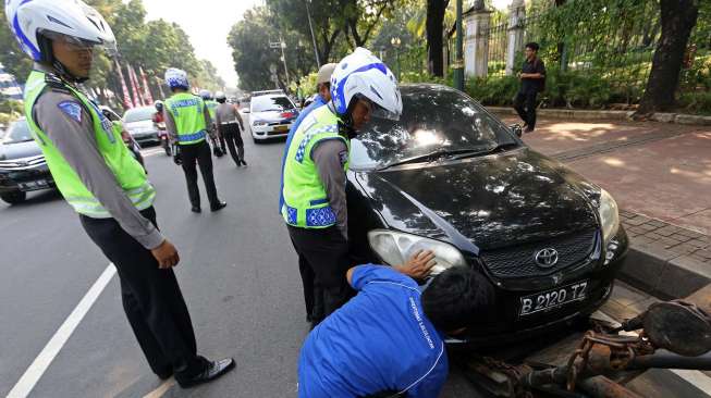 Petugas Polantas menertibkan kendaraan roda empat yang terparkir liar di sepanjang jalan Medan Merdeka Barat Jakarta, Senin (18/8). [suara.com/Kurniawan Mas'ud]