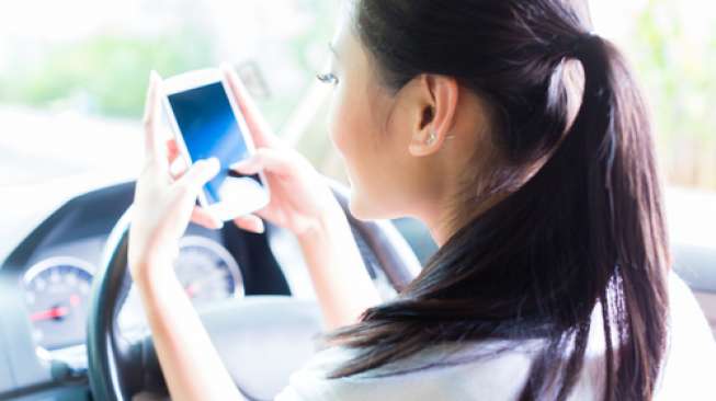 Ilustrasi perempuan memakai smartphone/ponsel sembari mengemudi. (Shutterstock)