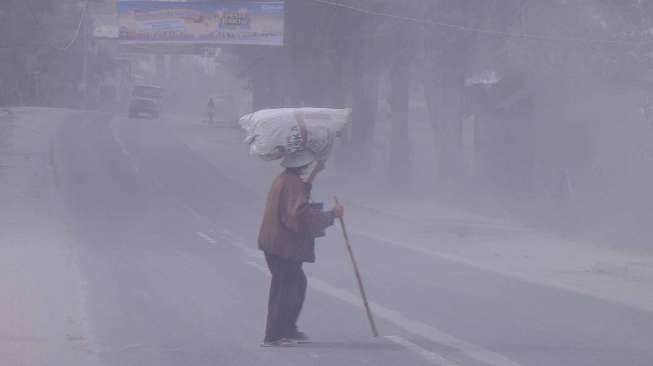 Seorang warga melintas disalah satu jalan yang tertutup debu vulkanik akibat dampak erupsi Gunung Sinabung, Kota Brastagi, Karo, Sumut, Kamis (9/10). [Antara/Tibta Perangin-angin]