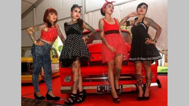 Beberapa orang perempuan bertato berpose di antara jejeran mobil-mobil klasik hot rod yang dipajang di lokasi acara Indonesia Greaser Party 2015, Jumat (10/4/2015), di Plaza Barat Senayan. [Suara.com/Oke Atmaja]