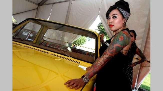 Beberapa orang perempuan bertato berpose di antara jejeran mobil-mobil klasik hot rod yang dipajang di lokasi acara Indonesia Greaser Party 2015, Jumat (10/4/2015), di Plaza Barat Senayan. [Suara.com/Oke Atmaja]