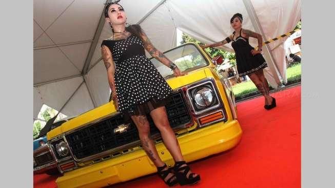 Beberapa orang perempuan bertato berpose di antara jejeran mobil-mobil klasik hot rod yang dipajang di lokasi acara Indonesia Greaser Party 2015, Jumat (10/4/2015), di Plaza Barat Senayan. [Suara.com/Oke Atmaja]