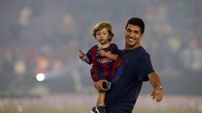 Luis Suarez menggendong putranya, Benjamin, saat rayakan keberhasilan Barcelona meraih treble (8/6) [Reuters/Albert Gea]