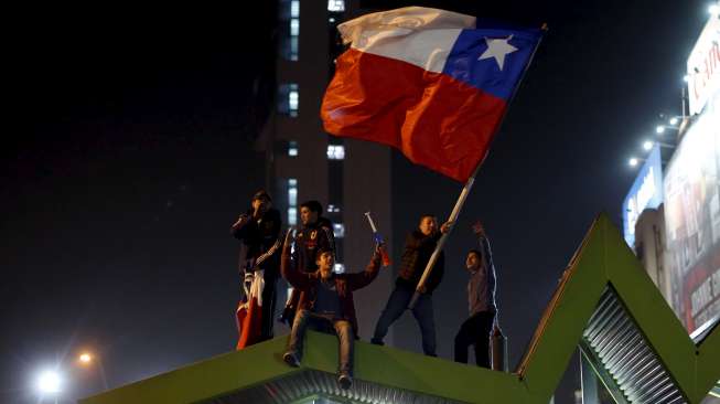 Fans Cile mengibarkan bendera Cile merayakan kemenangan skuatnya atas Uruguay di Santiago (25/6). Reuters/Pablo Sanhueza