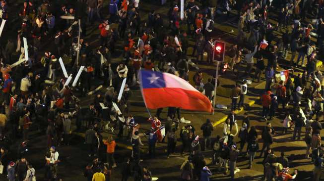 Seorang fans mengibarkan bendera Cile merayakan kemenangan skuatnya atas Uruguay di Santiago (25/6). Reuters/Pablo Sanhueza