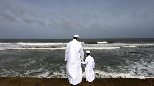 Seorang lelaki warga Muslim Sri Lanka bersama putranya, tampak berdiri di pantai, di pagi hari jelang salat Idul Fitri, di Kolombo, Sabtu (18/7/2015). [Reuters/Dinuka Liyanawatte]