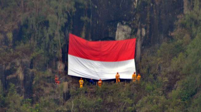 Sejumlah mahasiswa pecinta alam Bhiraswapa Unmer Madiun mengibarkan bendera Merah Putih berukuran 9x6 meter di tebing Sidoramping, Desa Ngancar, Plaosan, Magetan, Jatim, Senin (17/8/2015). [Antara/Fikri Yusuf]