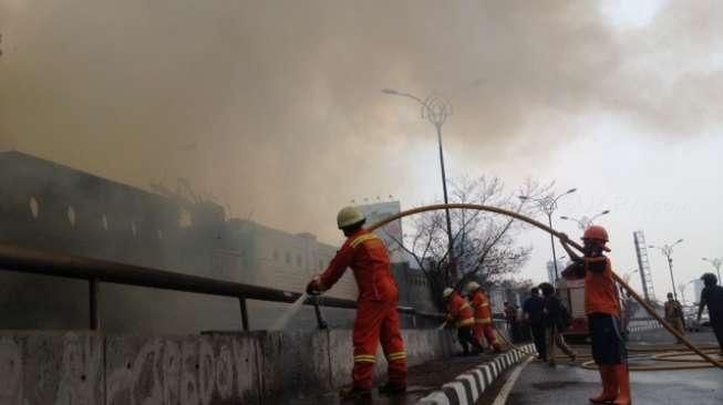 Petugas memadamkan api yang melalap permukiman liar di bawah jembatan layang Kuningan, Jakarta, Rabu (19/8). [Suara.com/Kurniawan Mas'ud]