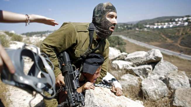 Seorang tentara Israel menangkap seorang bocah Palestina dalam aksi unjuk rasa menentang pembangunan permukiman Yahudi di Desa Nabi Saleh, Tepi Barat, hari Jumat (28/8/2015). [Reuters/Mohamad Torokman]