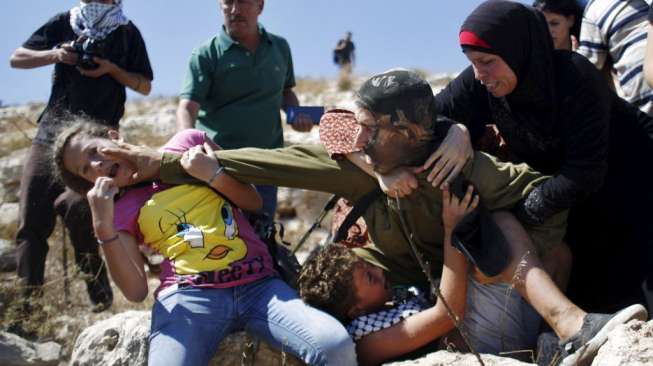 Seorang tentara Israel menangkap seorang bocah Palestina dalam aksi unjuk rasa menentang pembangunan permukiman Yahudi di Desa Nabi Saleh, Tepi Barat, hari Jumat (28/8/2015). [Reuters/Mohamad Torokman]