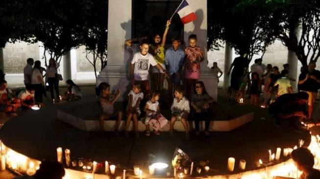 Anak-anak dengan bendera Prancis dan sejumlah orang dewasa memasang lilin di Plaza de Francia, Panama City, Sabtu (14/11/2015). [Reuters/Carlos Jasso]