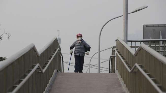 Warga berjalan melintasi jembatan di hari berkabut di Beijing, Cina, Senin (7/12). [Reuters/Jason Lee]