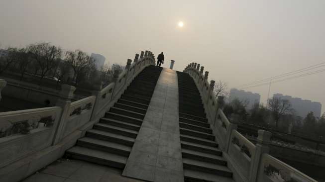 Warga berjalan melintasi jembatan di hari berkabut di Beijing, Cina, Senin (7/12). [Reuters/Jason Lee]