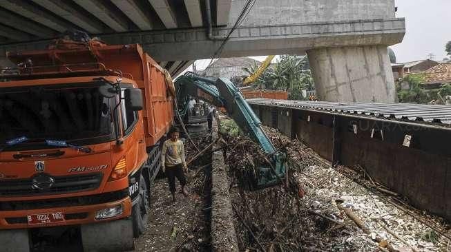 Menggunakan alat berat ekskavator, petugas membersihkan tumpukan sampah akibat hujan lebat di hulu, yang tersangkut di pondasi jembatan Jalan Kalibata Raya, Jakarta, Sabtu (5/3/2016). [Suara.com/Kurniawan Mas'ud]