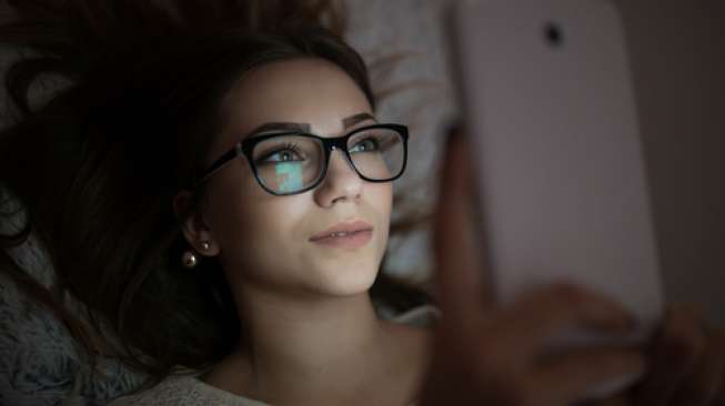 Ilustrasi seorang perempuan menggunakan ponsel menjelang tidur (Shutterstock).