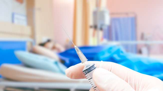 Ilustrasi seorang petugas medis sedang memegang jarum suntik di hadapan pasien (Shutterstock).