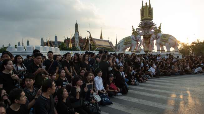 Ribuan khalayak berkumpul dekat Istana Kerajaan di Bangkok, sementara iring-iringan kendaraan pembawa jenazah Raja Thailand, Bhumibol Adulyadej, melintas di jalanan, Jumat (14/10/2016). [Roberto Schmidt/AFP]