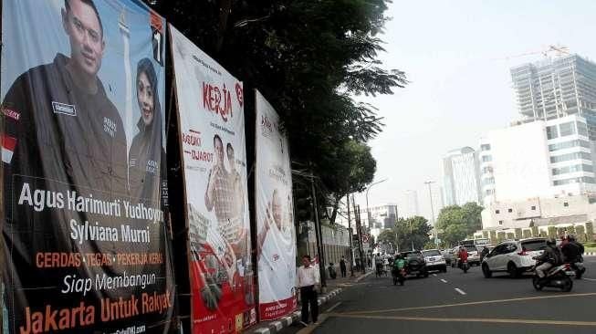 Pengguna jalan melintasi baliho bergambar tiga pasang calon Gubernur dan Wakil Gubernur DKI Jakarta di kawasan Tugu Tani, Jakarta, Selasa (22/11). [Suara.com/Oke Atmaja]