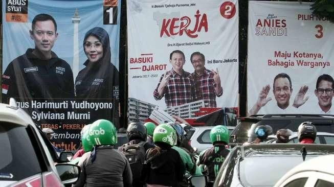 Pengguna jalan melintasi baliho bergambar tiga pasang calon Gubernur dan Wakil Gubernur DKI Jakarta di kawasan Tugu Tani, Jakarta, Selasa (22/11). [Suara.com/Oke Atmaja]