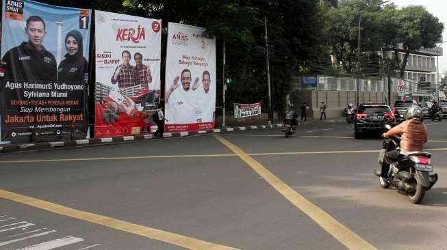 Pengguna jalan melintasi baliho bergambar tiga pasang calon Gubernur dan Wakil Gubernur DKI Jakarta di kawasan Tugu Tani, Jakarta, Selasa (22/11). [Suara.com/Oke Atmaja]