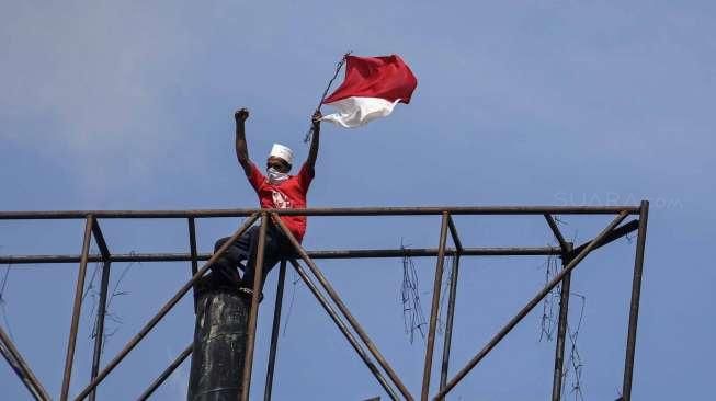 Seorang lelaki melakukan aksi nekat memanjat papan reklame di kawasan Harmoni, Jakarta, Selasa (20/12/2016). [Suara.com/Kurniawan Mas'ud]