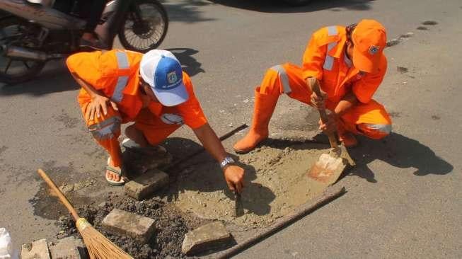 Petugas Penanganan Prasarana dan Sarana Umum (PPSU) menambal jalan berlubang di kawasan Kuningan, Jakarta, Jumat (17/2).