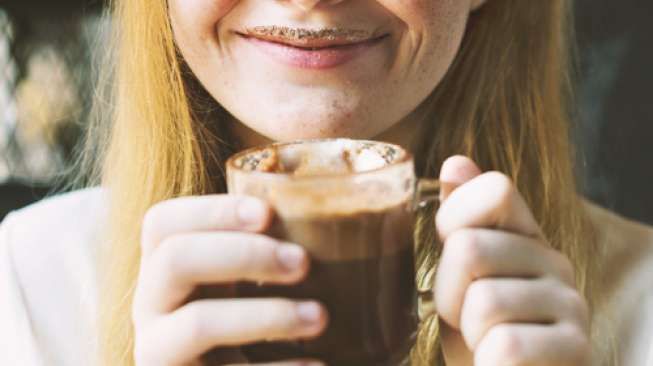 Seorang perempuan sedang menikmati cokelat panas yang tersaji dalam gelas. [shutterstock]